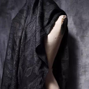 Puede incluir: Tela negra con estampado floral drapeada sobre un maniquí.