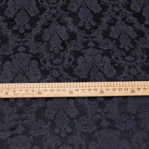 Pode incluir: Tecido escuro com um padr&atilde;o floral repetido. Uma r&eacute;gua de madeira, marcada em cent&iacute;metros, est&aacute; sobre o tecido, medindo at&eacute; 79 cm. O tecido tem um brilho sutil e um design detalhado e texturizado.