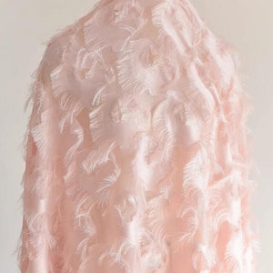 May include: A pale pink fabric with a textured, feathery design. The fabric has a soft, delicate look and feel.
