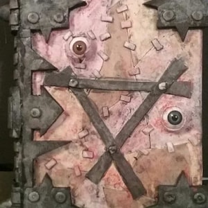 May include: A book with a stitched leather cover, metal accents, and two eyes. The book is decorated with a distressed, aged look.