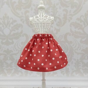 Può includere: Una gonna rossa con pois bianchi su un manichino bianco. La gonna ha un elastico in vita.