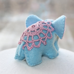 May include: A light blue felt elephant toy with pink crocheted trim and pink pearl accents.