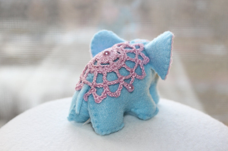 May include: A light blue felt elephant toy with pink crocheted trim and pink pearl accents.