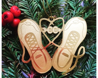 Puede incluir: Adorno navideño de metal dorado en forma de par de zapatillas para correr con una flecha y las letras "CC" en el centro.