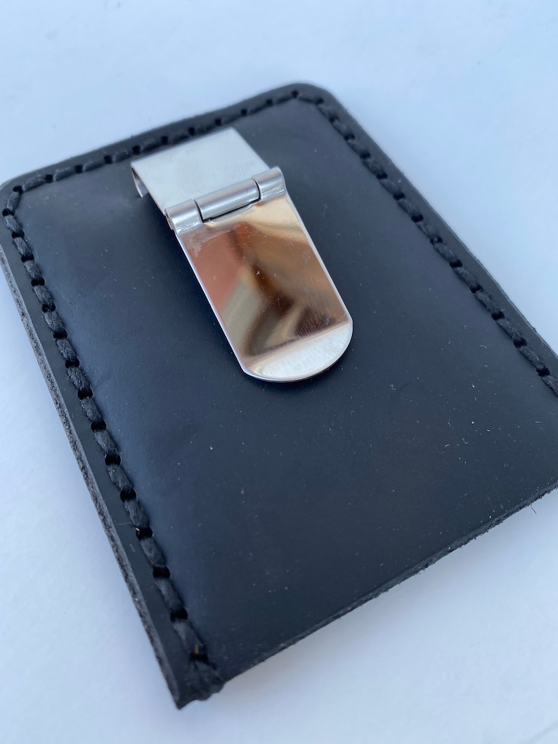 May include: A black leather money clip with a silver metal clip. The clip has a hinged design and a smooth, polished finish.