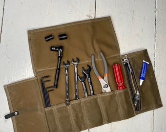 May include: A brown canvas roll-up tool bag with a zipper closure. The bag is open and contains various tools, including wrenches, pliers, screwdrivers, and Allen keys.