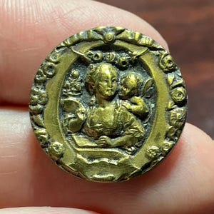 May include: A white ceramic mug with a black handle and the text "But First, Coffee" in a bold, black font. The mug is set against a blurred background, suggesting a cozy setting.