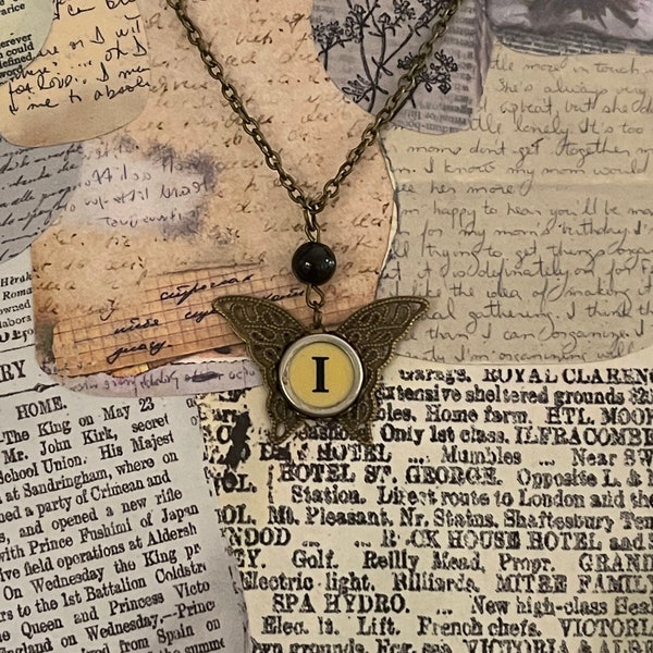 Vintage Cream Typewriter Key Letter "I” on a Brass Butterfly on 18" chain accented with a clear bead necklace. Other letters available.