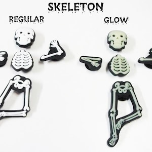 Op de afbeelding: Twee sets skelet-schoenbedels, &eacute;&eacute;n set is wit en de andere set gloeit in het donker. De bedels zijn gemaakt van plastic en zijn gevormd als een skelet. De bedels zijn gelabeld "Regular" en "Glow".