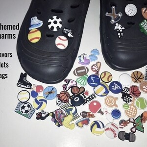May include: A collection of colorful sports-themed shoe charms featuring various balls, equipment, and athletic icons, displayed alongside two black clogs. The text "Sports themed shoe charms party favors bracelets gift bags" is visible on the left.