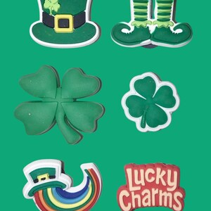 Può includere: Una collezione di ciondoli a tema San Patrizio su sfondo verde. I ciondoli includono un cappello verde con un trifoglio, stivali da folletto verdi, trifogli, un arcobaleno con un pentolone d'oro e il testo "Lucky Charms".