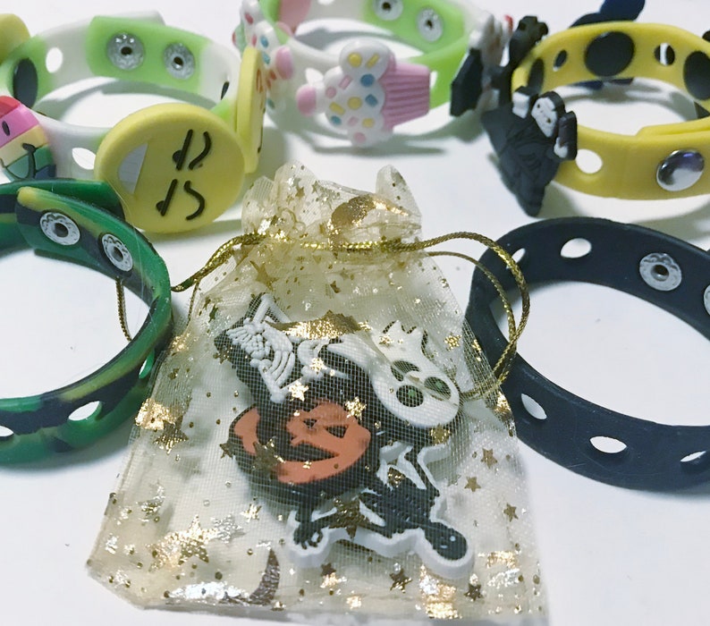 Puede incluir: Una colecci&oacute;n de pulseras de silicona a presi&oacute;n de colores con varios dijes decorativos, incluyendo una carita sonriente, una magdalena y figuras de Halloween. Una peque&ntilde;a bolsa con ribete dorado contiene dijes adicionales.