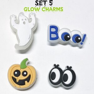 Op de afbeelding: Set van vijf glow-in-the-dark Halloween schoenbedels. De bedels omvatten een spook, een pompoen, twee paar oogjes en het woord "Boo!" met oogjes.