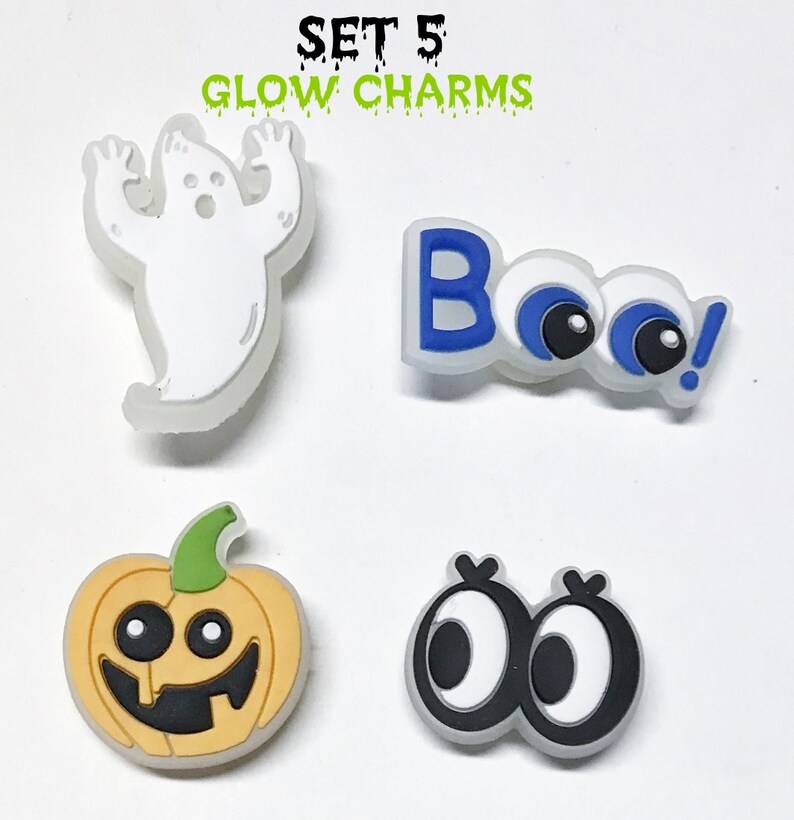Op de afbeelding: Set van vijf glow-in-the-dark Halloween schoenbedels. De bedels omvatten een spook, een pompoen, twee paar oogjes en het woord "Boo!" met oogjes.