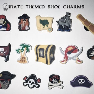 May include: A collection of pirate-themed shoe charms. The charms include a pirate, a map, a ship, a spyglass, a pirate flag, a treasure chest, crossed swords, a skull, a pirate hat, and a palm tree.