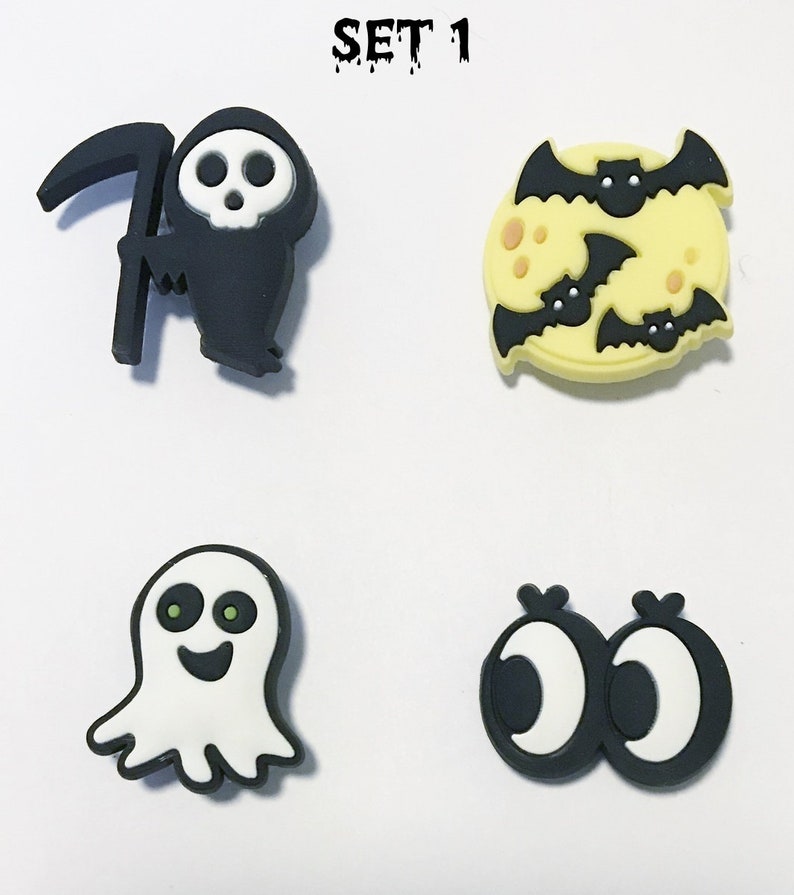 Op de afbeelding: Set van vier Halloween-schoenbedels. De bedels zijn zwart, wit en geel en bevatten een Grim Reaper, een geest, een maan met vleermuizen en twee oogjes.