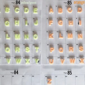 Puede incluir: Dos p&aacute;ginas de letras del alfabeto en una cuadr&iacute;cula. Una p&aacute;gina presenta letras amarillas/verdes, la otra naranja. Cada letra es un dise&ntilde;o hinchado y tridimensional. Las p&aacute;ginas est&aacute;n etiquetadas como "P&aacute;gina 84 amarillo/verde" y "P&aacute;gina 85 naranja".