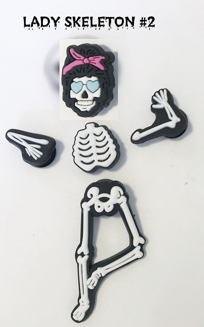 Op de afbeelding: Een set van vijf zwarte en witte skeletcharms met een roze hoofdband. De charms omvatten een schedel met een zonnebril, een ribbenkast, twee armen en een paar benen.