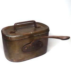 May include: A vintage copper cooking pot with a hinged lid and a handle. The pot has a worn, aged patina and a small, oval-shaped handle on the side.
