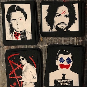 May include: Four black and white patches with images of famous criminals. The patches are on a wooden surface. The first patch shows a man with a red cross on his forehead. The second patch shows a man with a red cross on his forehead. The third patch shows a man with a red pentagram and a red circle around him. The fourth patch shows a man with red and blue makeup on his face. The text on the fourth patch reads "Police Department Waterloo, Iowa 18022".