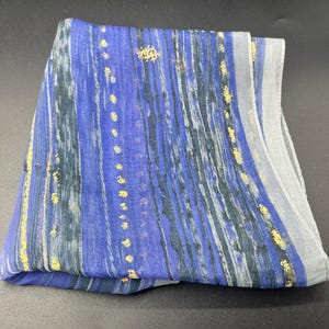 May include: Folded blue scarf with vertical stripes in shades of blue, gray, and black. Gold flecks are scattered throughout the design. The scarf is made of a lightweight fabric.