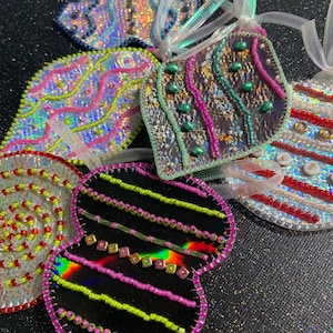 May include: A collection of iridescent beaded ornaments in various shapes, including a heart, a teardrop, and a swirl design. The ornaments are decorated with colorful beads and sequins, creating a festive and sparkly look.