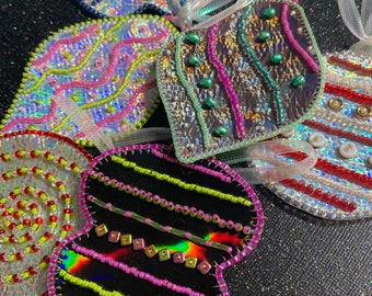 May include: A collection of iridescent beaded ornaments in various shapes, including a heart, a teardrop, and a swirl design. The ornaments are decorated with colourful beads and sequins, creating a festive and sparkly look.