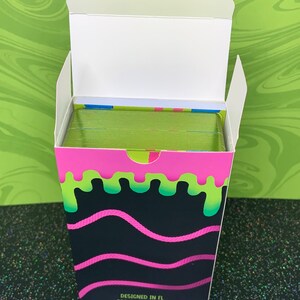May include: A box of playing cards with a green, pink and black slime design. The box says "Designed in FL Printed in China".