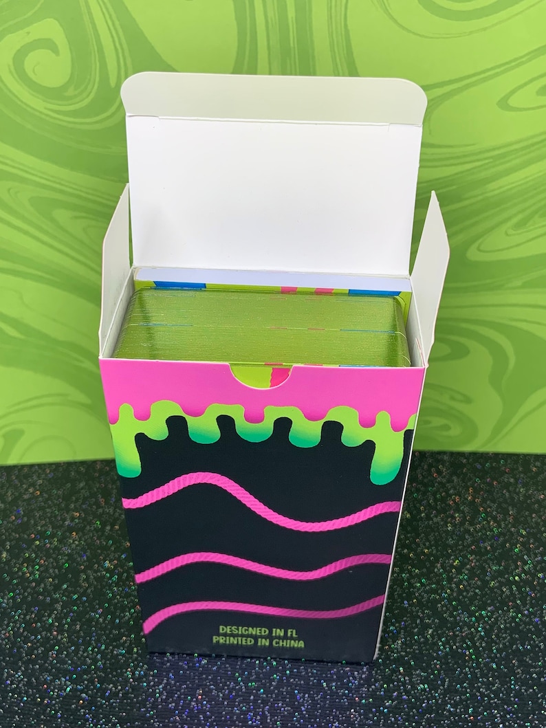 May include: A box of playing cards with a green, pink and black slime design. The box says "Designed in FL Printed in China".