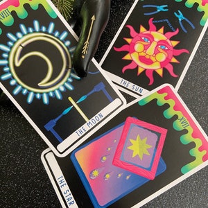 May include: Three tarot cards with a neon-coloured design. The cards are The Moon, The Star, and The Sun. The Moon card features a crescent moon with a glowing halo, The Star card shows a star in a frame with shooting stars, and The Sun card depicts a smiling sun with a chain and pliers.