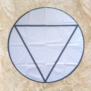 May include: A white round yoga mat with a black triangle design. The mat has a black border.