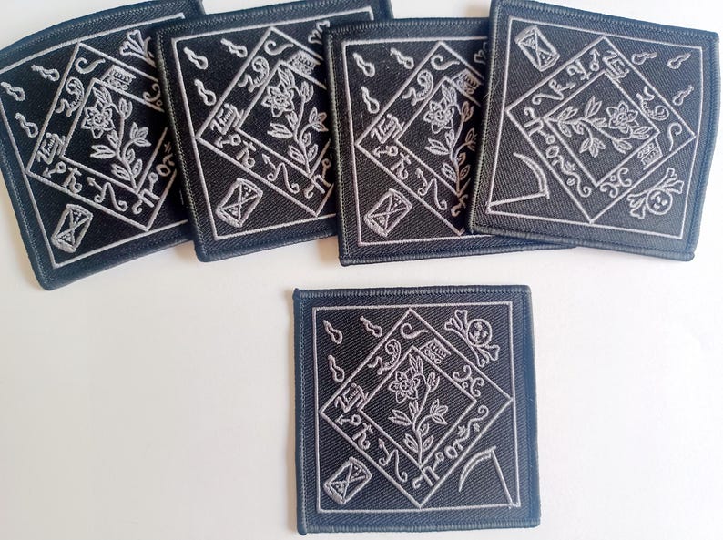May include: Five black square patches with white embroidered designs. Each patch features a stylized flower with a stem and leaves, a crescent moon, a scythe, a skull, and an hourglass. The patches are approximately 4 inches by 4 inches.