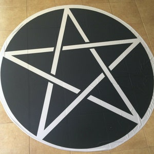 May include: A black and white pentagram design on a round, white-edged, black fabric.