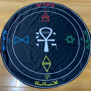 Puede incluir: Un paño circular negro con símbolos blancos y de colores. Los símbolos incluyen una estrella de David, un ankh, un triángulo y un triángulo doble. El texto "10/omega" está escrito en blanco sobre el ankh. El paño tiene un borde blanco con texto hebreo alrededor del borde.