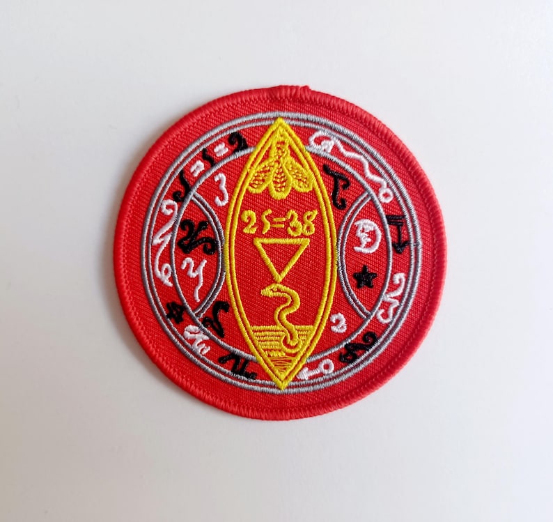 Peut inclure: Patch brod&eacute; rouge avec un symbole jaune et noir &agrave; l'int&eacute;rieur d'un cercle. Le symbole repr&eacute;sente un serpent, un triangle et le texte "25=38". Le cercle a un motif gris et blanc avec du texte noir.