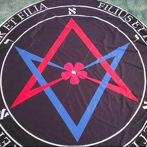 May include: A black circular textile with white text around the edge, reading "PATER ET FILIA, MATER ET FILIA, FILIUS ET FILIA." The design features a red and blue star-like shape with a pink flower in the center.