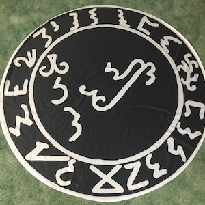 May include: A black circle with white symbols and a white design in the center. The circle is on a green surface.