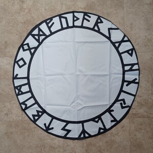 May include: A white circular tapestry with a black border featuring a repeating pattern of Viking runes. The tapestry is made of a soft, woven fabric.