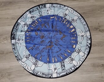 May include: A round blue and white tapestry with a circular design of stylized figures. The figures are arranged in a circle around a central blue circle with a pattern of stylized figures and symbols.