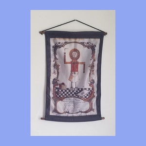 Puede incluir: Un tapiz de estilo vintage que presenta una figura estilizada con una cabeza en forma de sol, sosteniendo un pincel. La figura se encuentra sobre una plataforma a cuadros con una pancarta debajo que dice "A Free Mason, Founded on the Principles of his Order."