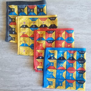 May include: Four tarot cloth squares with different coloured backgrounds. The squares are black, yellow, red, and blue. Each square has a grid of 16 squares with tarot symbols and Hebrew letters. The symbols include the Star, Hierophant, Death, Justice, Fool, Lovers, World, Chariot, Devil, Moon, Hermit, and more.