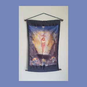 May include: A black fabric wall tapestry with a colorful image of a winged figure rising from a tomb. Three figures kneel in front of the tomb, looking up at the winged figure. The tapestry is hanging from a wooden rod.