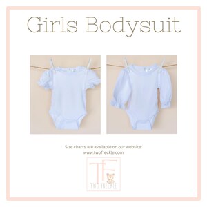 The image is a collage of two photos of white baby bodysuits hanging on a clothesline. The text above the images reads "Girls Bodysuit" and below the images, it says "Size charts are available on our website: www.twofreckle.com".