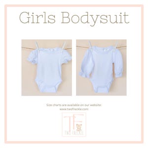 The image is a collage of two photos of white baby bodysuits hanging on a clothesline. The text above the images reads "Girls Bodysuit" and below the images, it says "Size charts are available on our website: www.twofreckle.com".