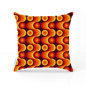 May include: Square cushion with a retro design. The cushion features a repeating pattern of orange, yellow, and red concentric circles on a dark purple background. The cushion has a tag that reads "LEO & CAL".