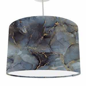 May include: A pendant lampshade with a marbled design. The lampshade features a blend of dark blue, grey, and gold colours. The gold accents create a striking contrast against the darker hues. The lampshade is suspended from a white cord.