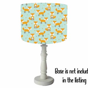 May include: A white table lamp with a light blue lampshade featuring a repeating pattern of orange foxes. The lampshade has a white trim around the top and bottom. The base is not included in the listing.