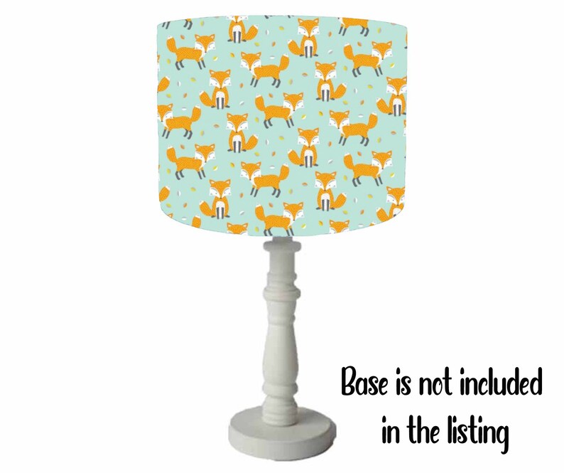 May include: A white table lamp with a light blue lampshade featuring a repeating pattern of orange foxes. The lampshade has a white trim around the top and bottom. The base is not included in the listing.