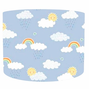 May include: A cylindrical lampshade with a pale blue backdrop, decorated with a repeating pattern of smiling suns, white clouds, rainbows, raindrops, and butterflies. The design is playful and suitable for a child's room.