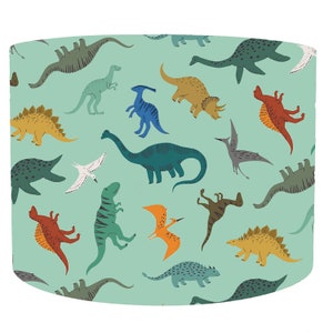 May include: A lampshade with a repeating pattern of colourful dinosaurs on a light teal background. The dinosaurs are in shades of green, blue, yellow, orange, and brown. The design includes a variety of dinosaur species.